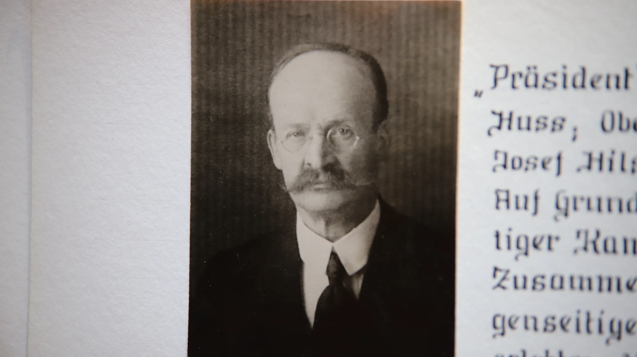 Aufgeschlagene Chronikseite: links das eingeklebte Porträt eines älteren Herrn mit Brille und Schnurrbart im dunklen Anzug, rechts daneben handschriftliche Zeilen in alter deutscher Schrift.