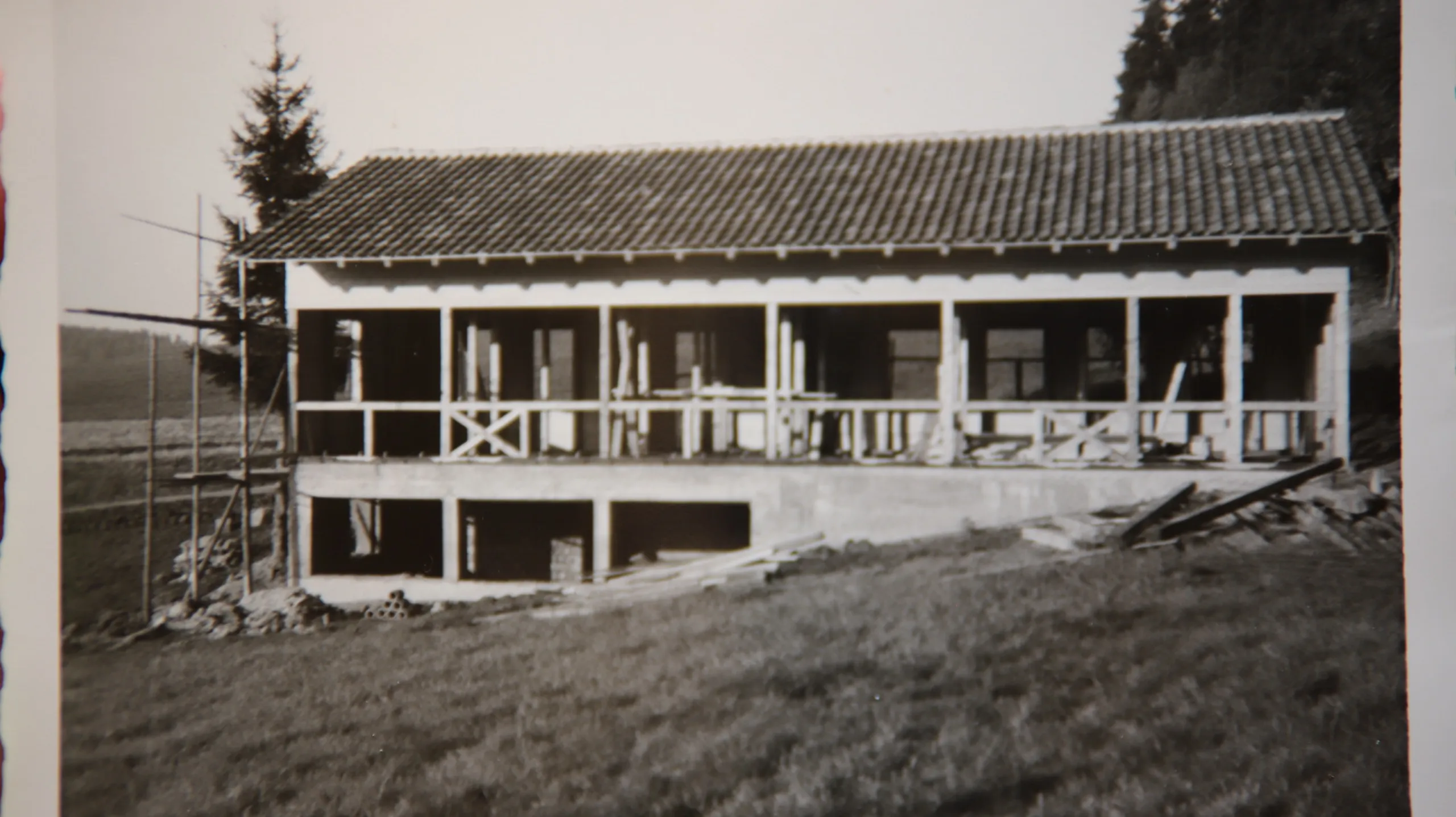 Schwarzweißaufnahme des Rohbaus: ein zweigeschossiger Bau mit offener Pfeilerreihe im Obergeschoss, das Dach ist gedeckt, am Giebel steht noch ein Gerüst.
