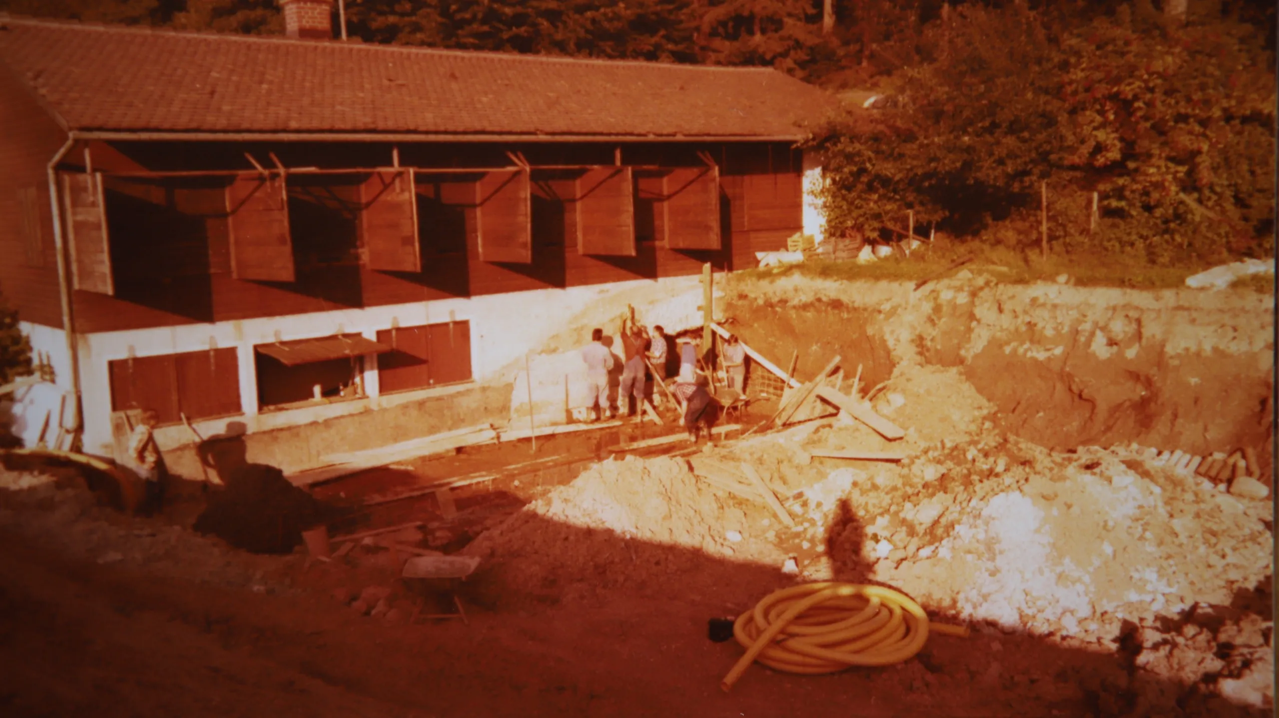 Farbaufnahme der Baustelle: die neue Standanlage mit offenen Betonkammern, davor aufgewühlte Erde, Schläuche und mehrere arbeitende Personen.
