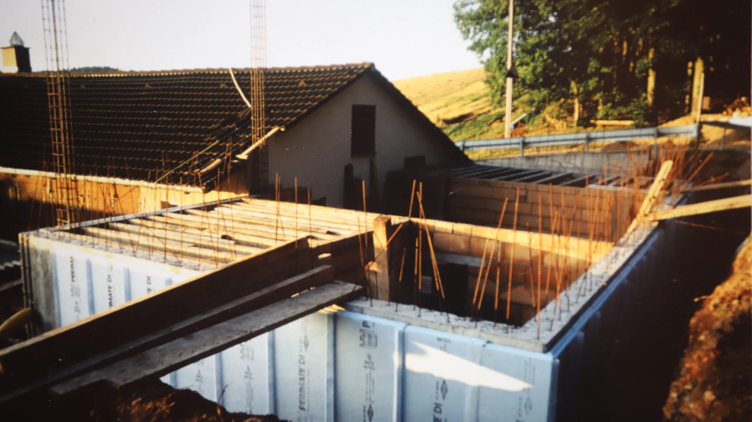 Farbaufnahme einer Baustelle: bewehrte Betonwände und blaue Dämmplatten für Küche und Toiletten, darüber ragt ein schwarzer Stahlträger.
