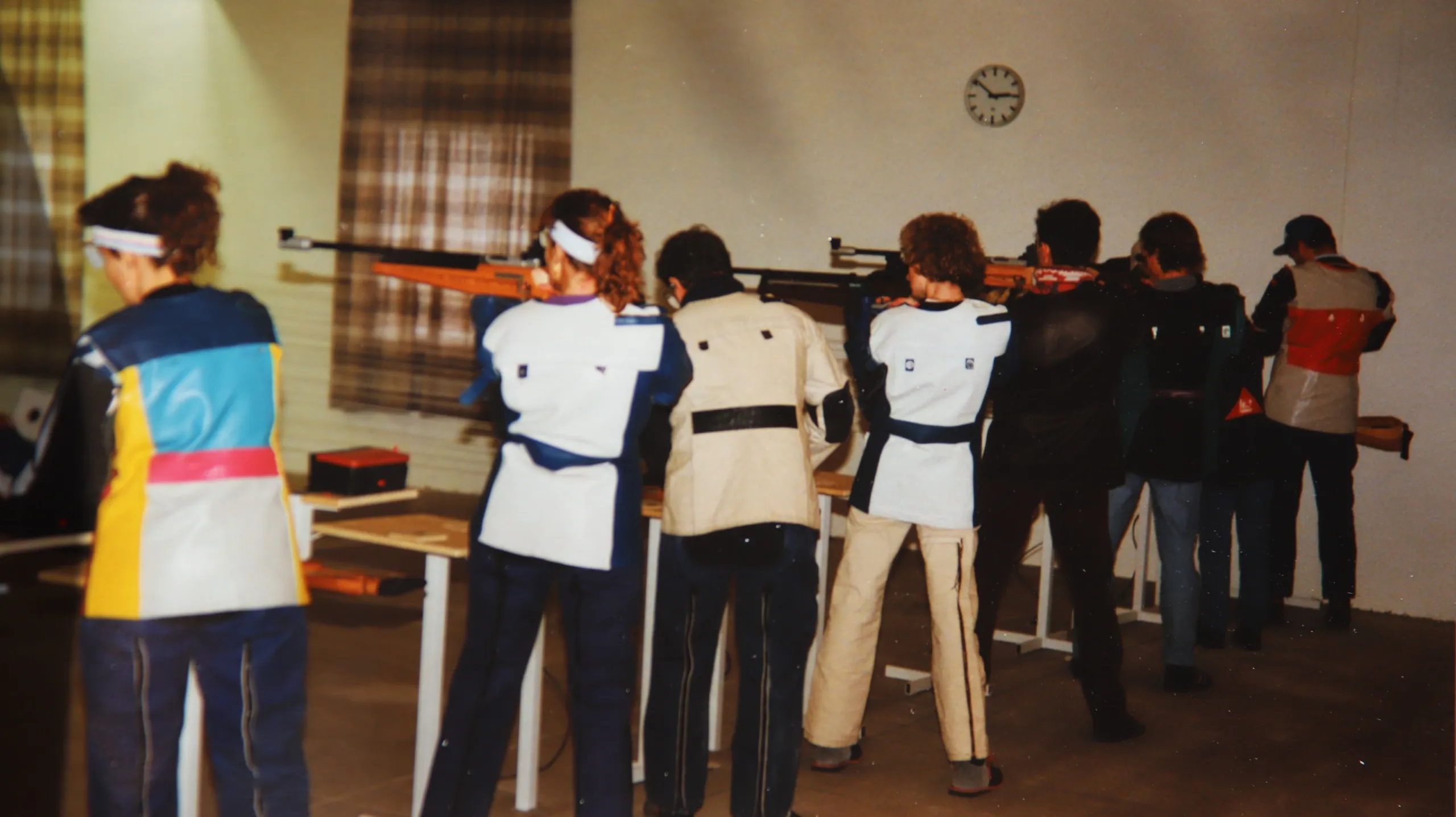 Farbaufnahme in der neuen Halle: sechs Schützinnen und Schützen in Schießkleidung stehen an den Ständen und legen mit dem Luftgewehr an, an der Wand hängt eine Uhr.