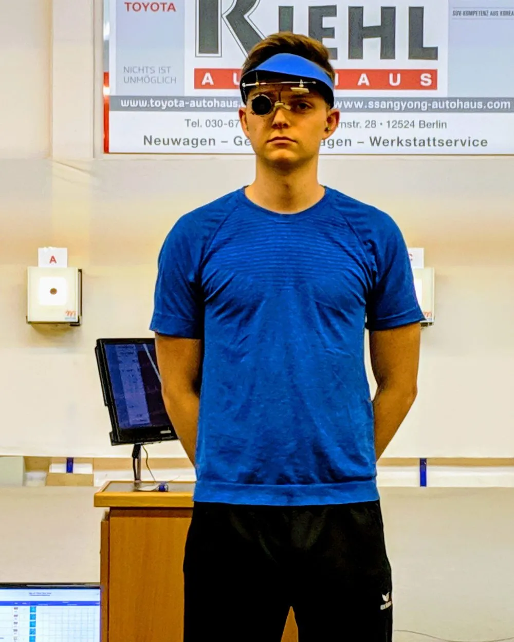 Luca Schröder im Wettkampf: blaues Trikot, Schießbrille, den Blick zur Scheibe gerichtet, daneben der Bildschirm der Trefferanzeige.