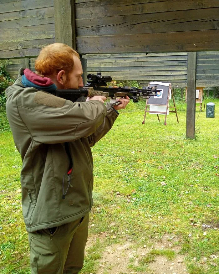 Ein Schütze legt am Außenstand mit der Armbrust an, vor ihm auf der Wiese Zielscheiben auf Ständern.