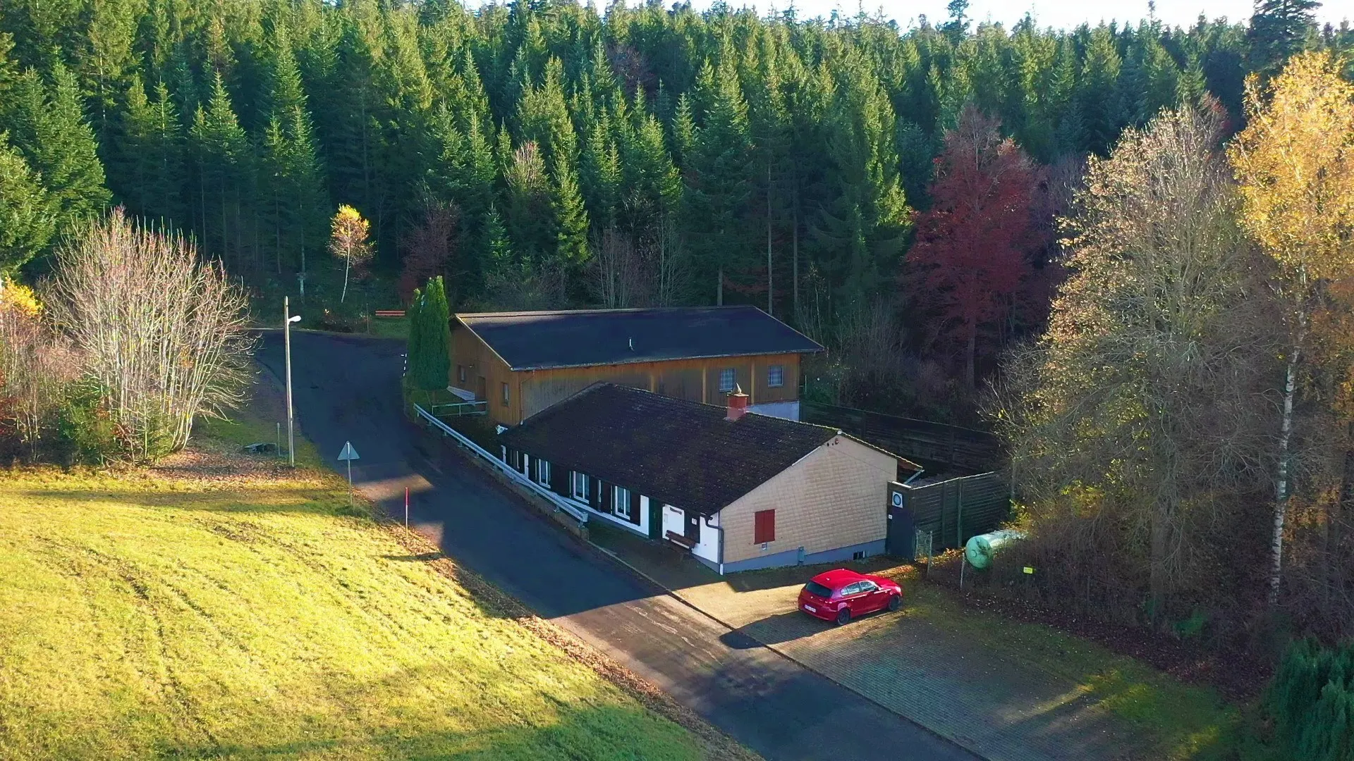 Das Schützenhaus der Schützengilde St. Georgen von oben: zwei langgestreckte Gebäude an einer Waldlichtung, ringsum Nadelwald in Herbstfärbung.